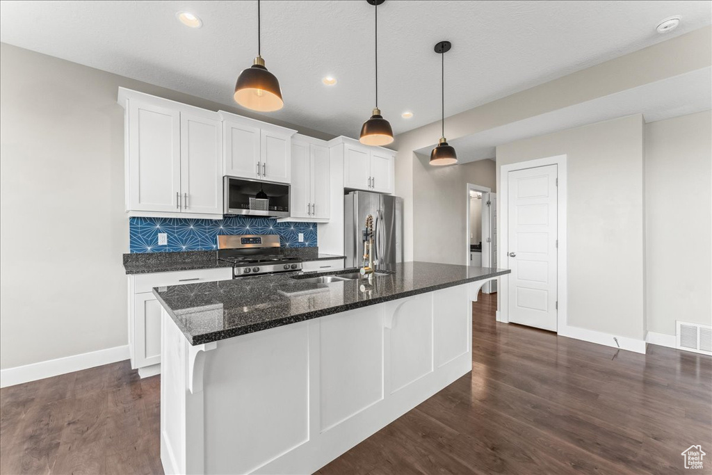 Kitchen featuring appliances with stainless steel finishes, white cabinetry, dark hardwood / wood-style flooring, and pendant lighting