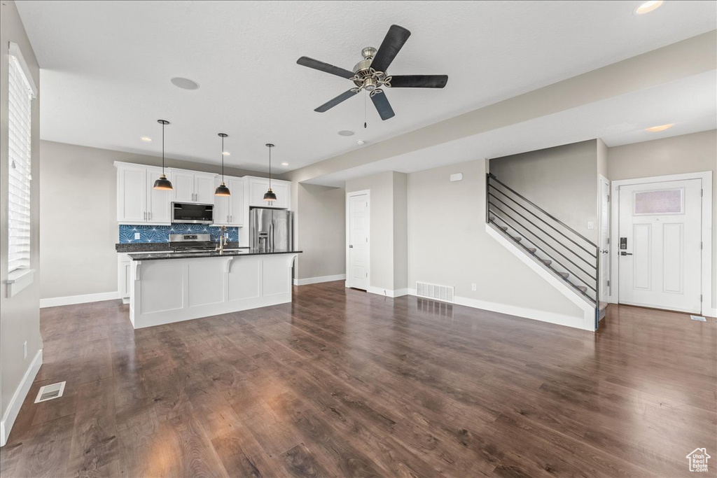 Kitchen featuring ceiling fan, a center island with sink, appliances with stainless steel finishes, white cabinets, and dark hardwood / wood-style floors