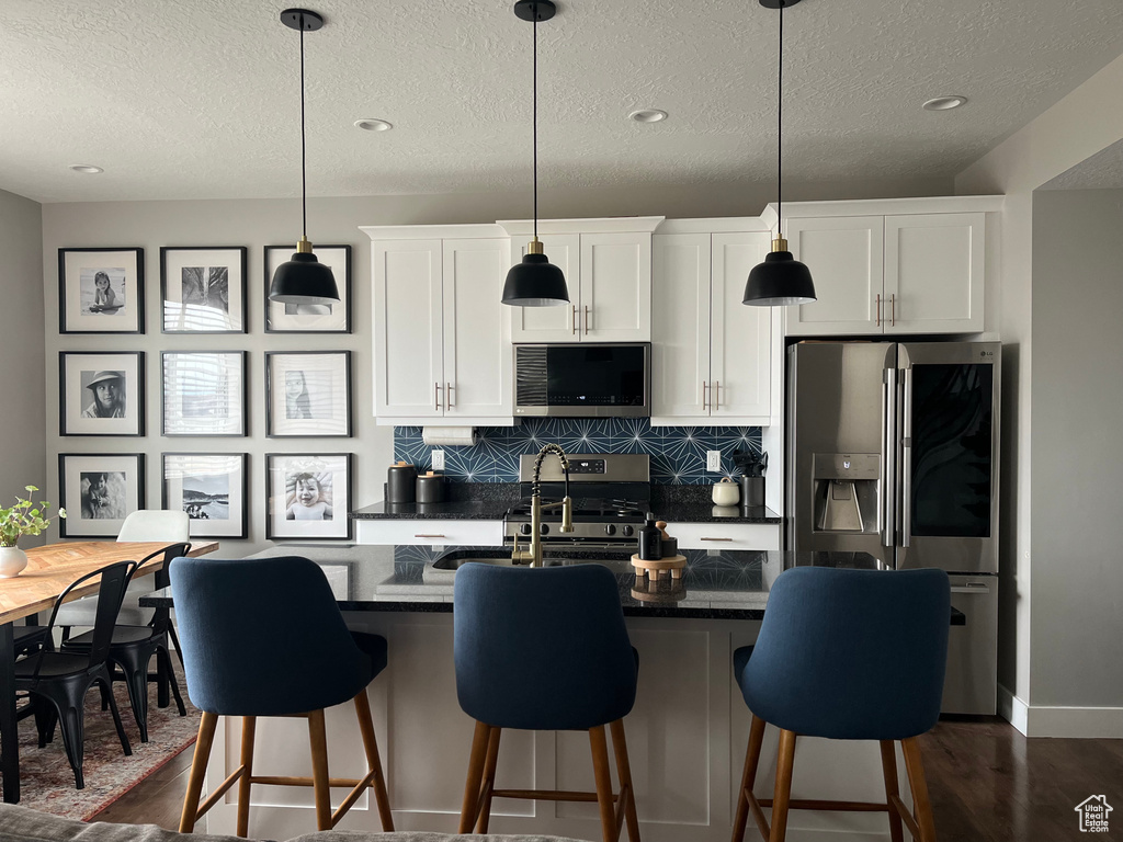 Kitchen featuring white cabinets, a kitchen bar, pendant lighting, and stainless steel appliances