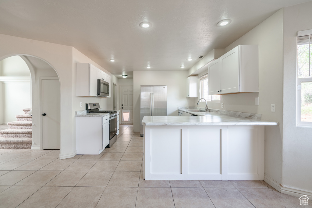 Kitchen featuring stainless steel appliances, white cabinetry, light tile floors, and a wealth of natural light