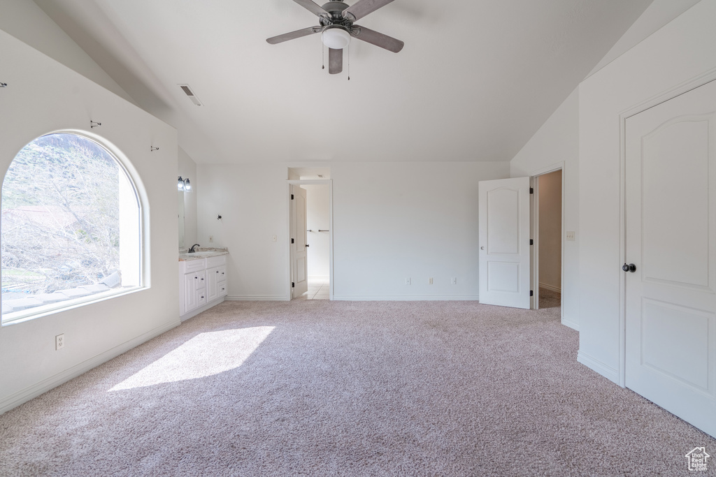 Unfurnished bedroom with connected bathroom, sink, ceiling fan, light carpet, and lofted ceiling