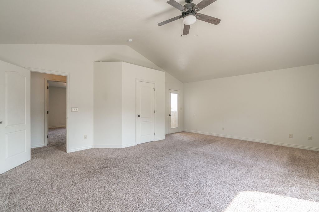Empty room featuring light colored carpet, ceiling fan, and lofted ceiling