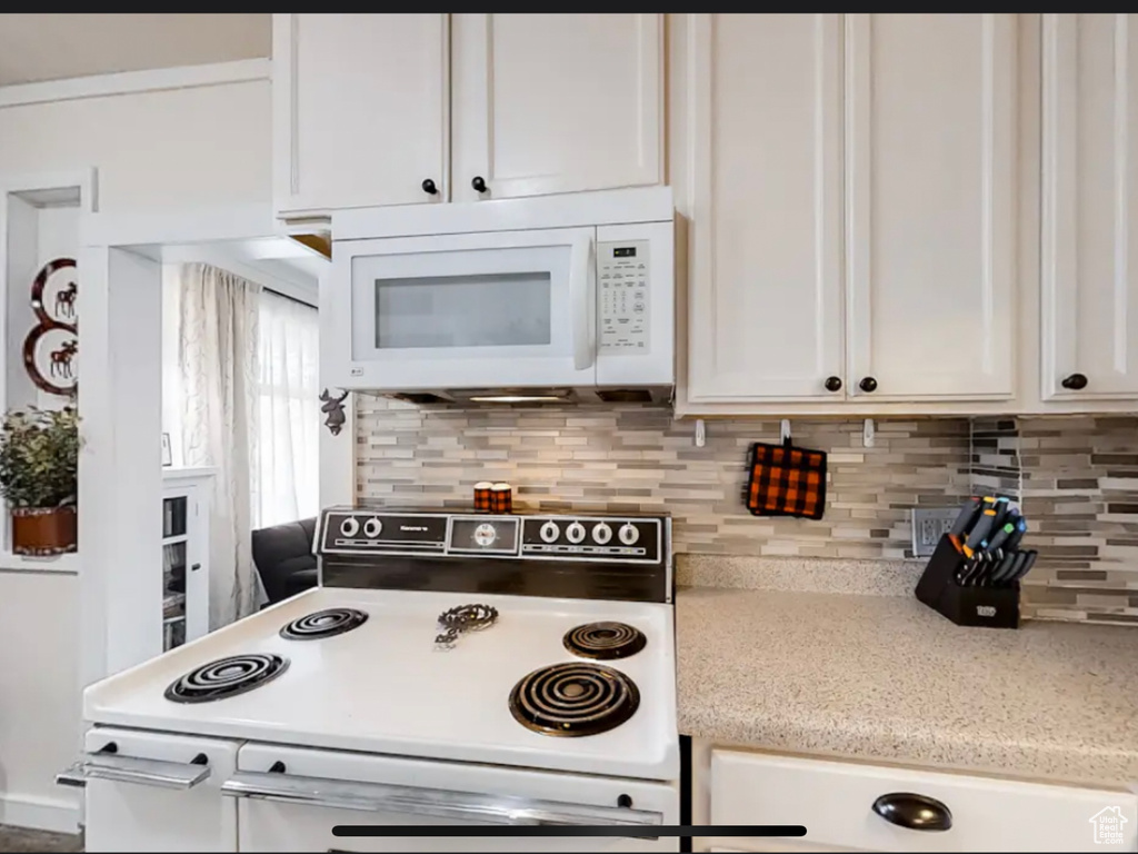 Kitchen with white appliances, white cabinetry, and backsplash
