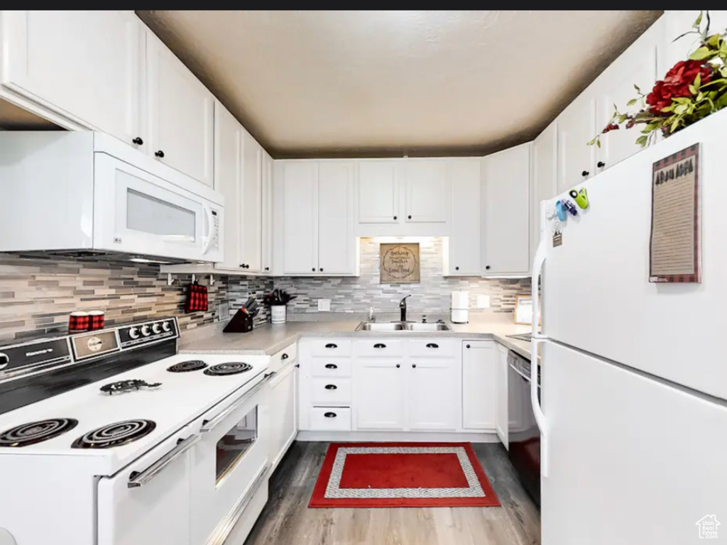 Kitchen with white appliances, sink, light hardwood / wood-style floors, tasteful backsplash, and white cabinetry