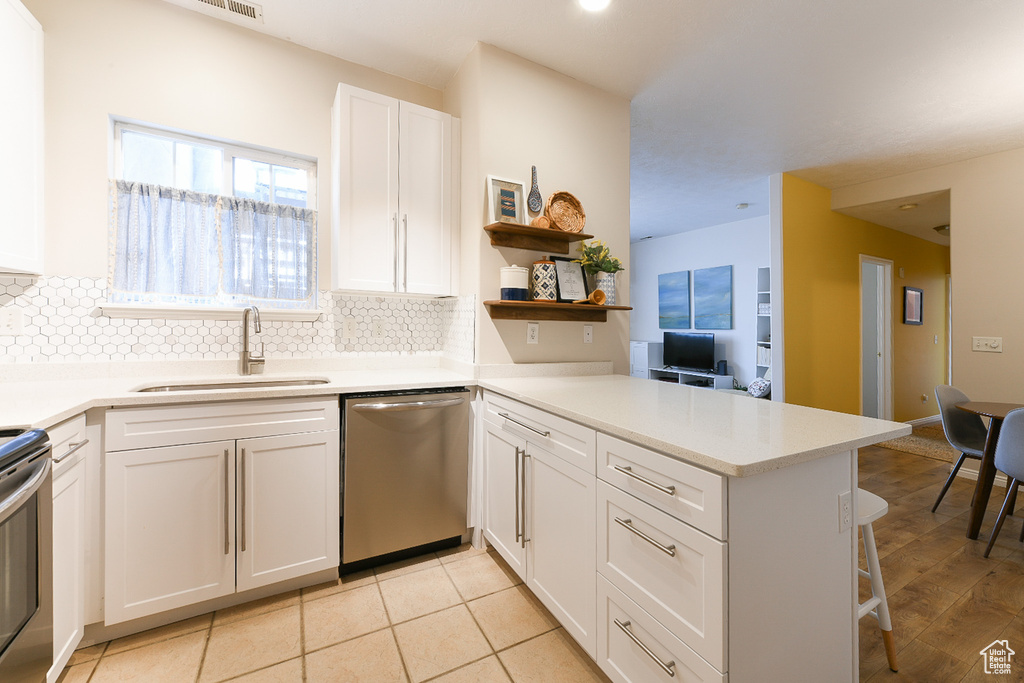 Kitchen featuring stainless steel dishwasher, kitchen peninsula, tasteful backsplash, white cabinetry, and sink