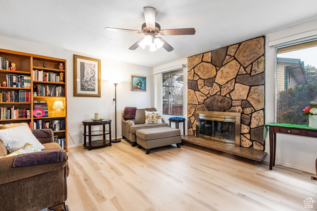Living room featuring light hardwood / wood-style floors, ceiling fan, and a stone fireplace