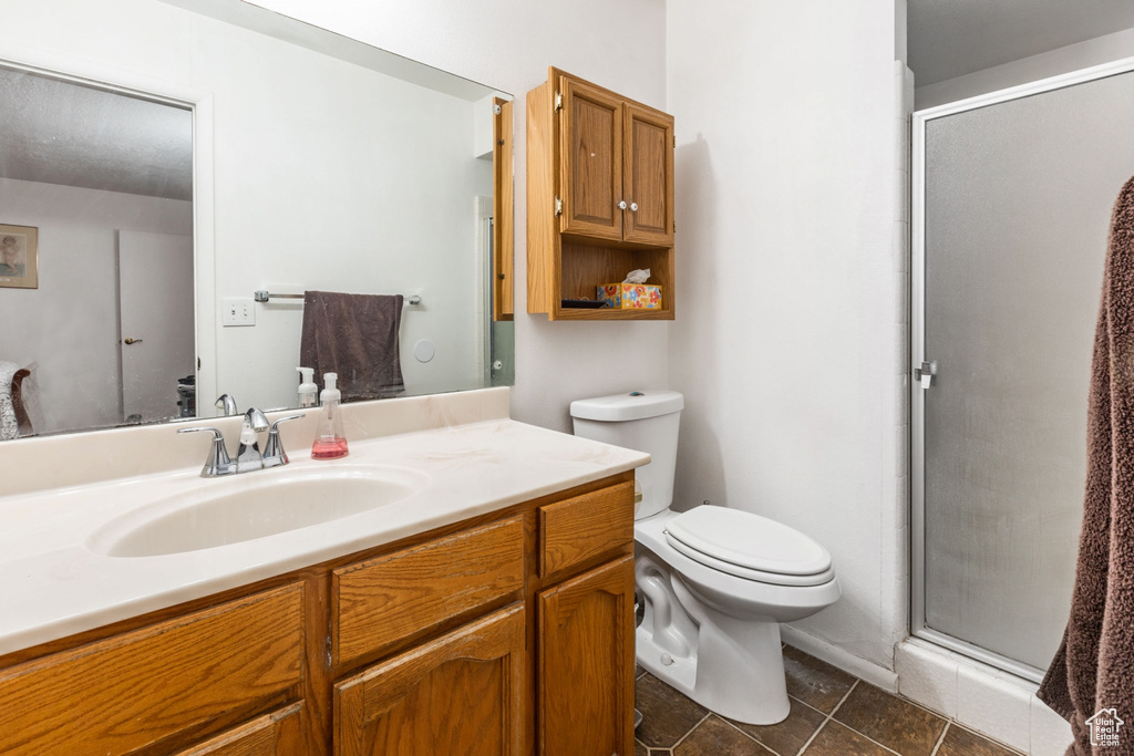 Bathroom with tile floors, a shower with shower door, vanity with extensive cabinet space, and toilet
