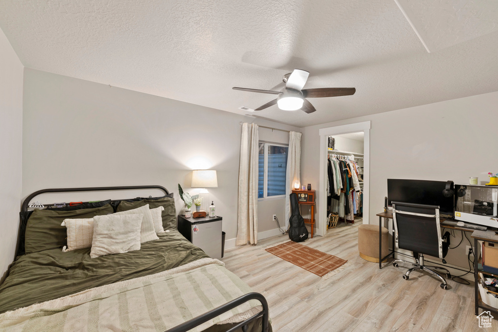 Bedroom with a closet, a walk in closet, ceiling fan, light hardwood / wood-style flooring, and a textured ceiling