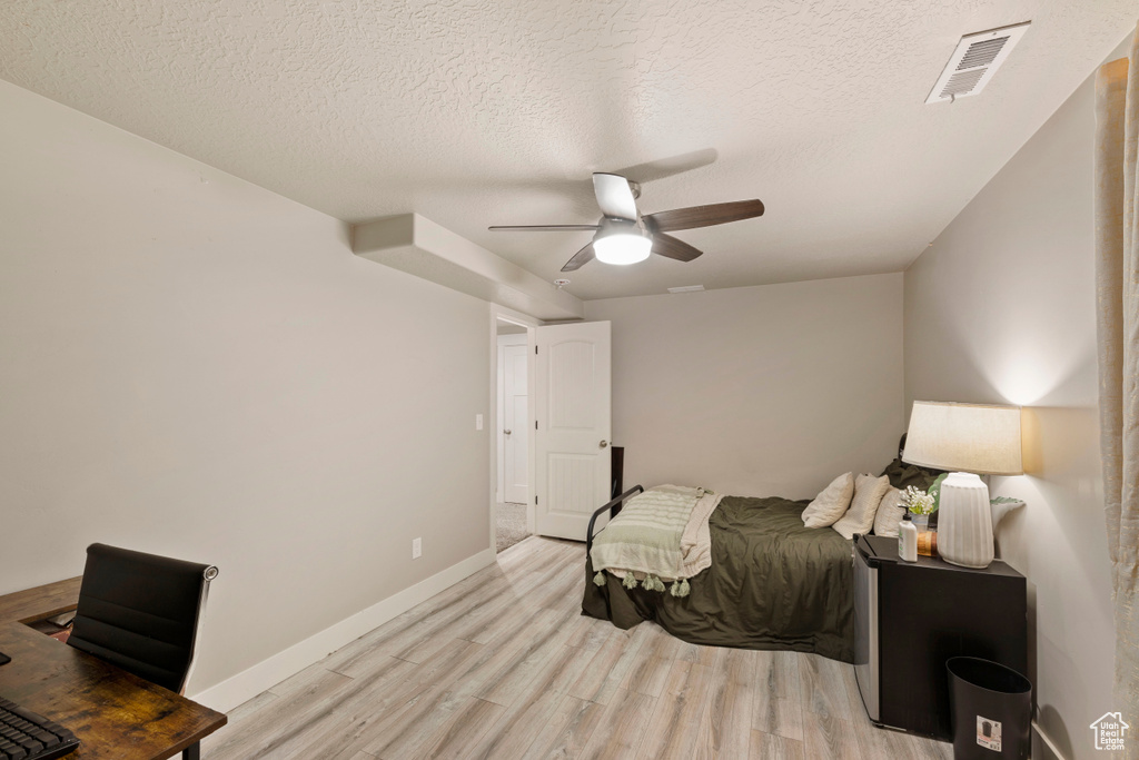 Bedroom with a textured ceiling, ceiling fan, and light hardwood / wood-style flooring