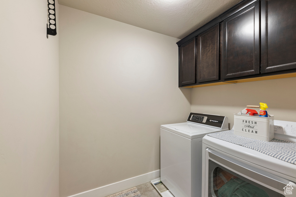 Clothes washing area with light tile floors, cabinets, and washer and dryer