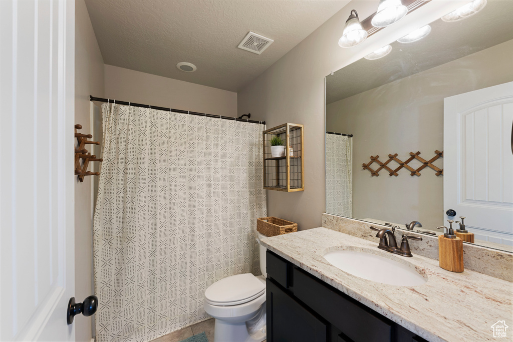 Bathroom featuring a textured ceiling, vanity with extensive cabinet space, and toilet