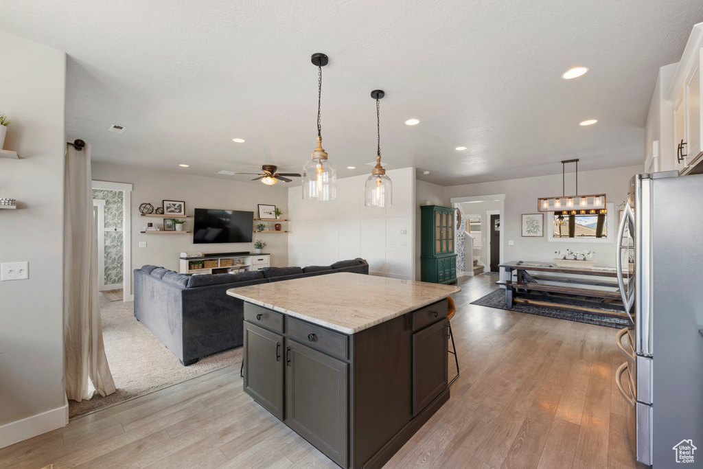 Kitchen with white cabinets, hanging light fixtures, stainless steel refrigerator, and light wood-type flooring
