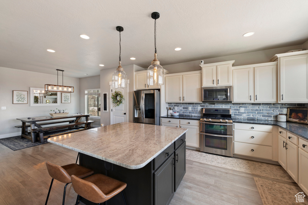 Kitchen with light wood-type flooring, dark stone countertops, decorative light fixtures, and appliances with stainless steel finishes