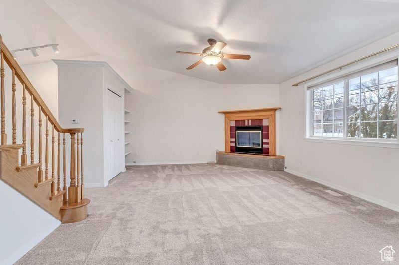 Unfurnished living room with light carpet, rail lighting, a fireplace, and ceiling fan