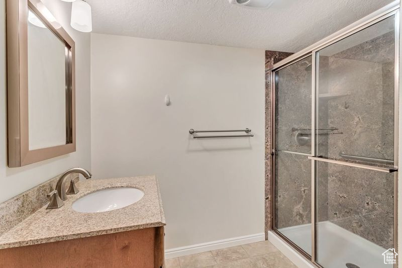 Bathroom with an enclosed shower, a textured ceiling, tile floors, and vanity with extensive cabinet space