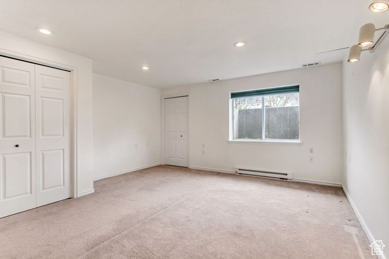 Unfurnished room featuring light colored carpet and a baseboard radiator