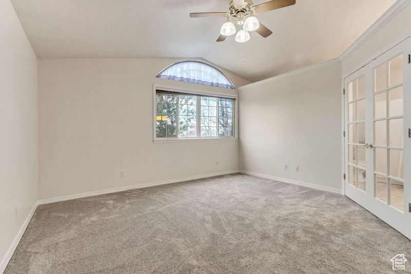 Spare room featuring light colored carpet, vaulted ceiling, ceiling fan, and french doors