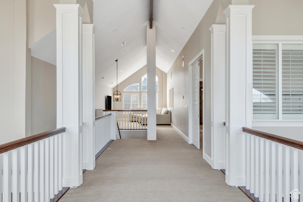 Hallway with light carpet, high vaulted ceiling, radiator heating unit, and decorative columns