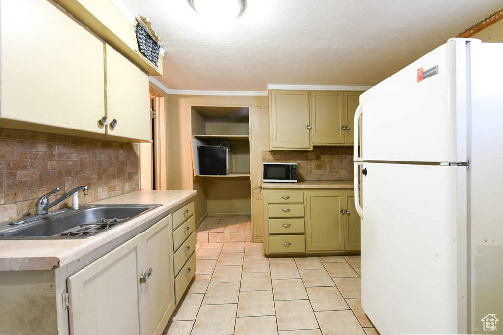 Kitchen with white fridge, sink, light tile floors, tasteful backsplash, and ornamental molding