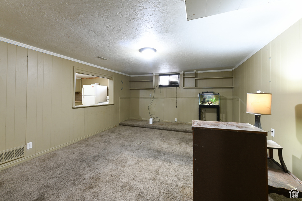 Basement featuring light colored carpet, a textured ceiling, white refrigerator, and crown molding