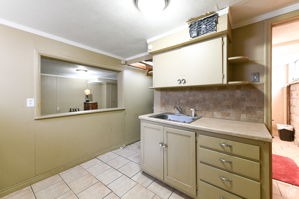 Kitchen featuring light tile floors, a textured ceiling, tasteful backsplash, ornamental molding, and sink