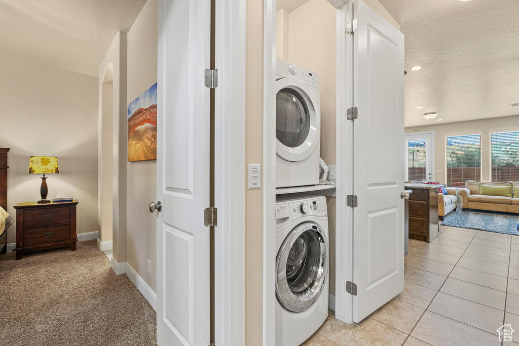 Laundry room featuring stacked washing maching and dryer and light colored carpet