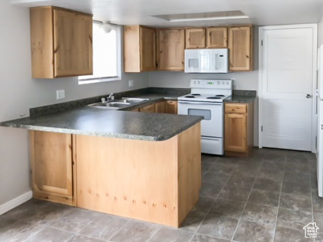 Kitchen featuring white appliances, kitchen peninsula, dark tile flooring, and sink