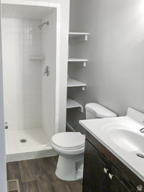 Bathroom with hardwood / wood-style floors, toilet, vanity, and tiled shower