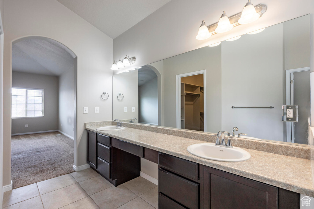 Bathroom featuring tile flooring, vaulted ceiling, large vanity, and dual sinks