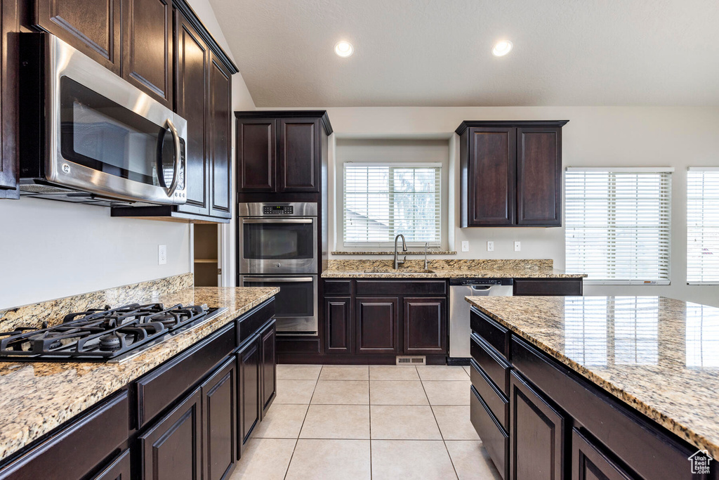 Kitchen with appliances with stainless steel finishes, dark brown cabinetry, sink, and light tile floors