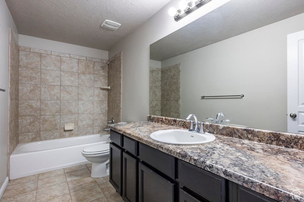 Full bathroom with tile flooring, tiled shower / bath, a textured ceiling, oversized vanity, and toilet