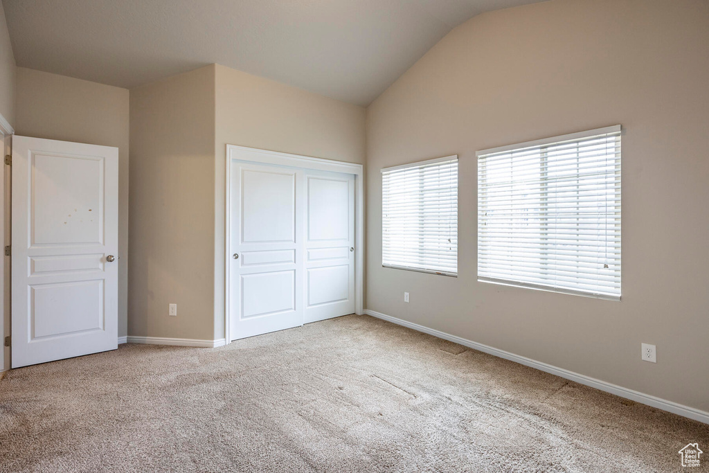 Unfurnished bedroom featuring light carpet, lofted ceiling, and a closet
