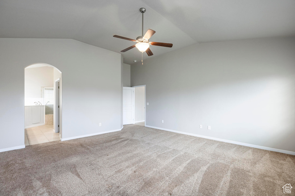 Unfurnished bedroom featuring high vaulted ceiling, ensuite bath, light colored carpet, and ceiling fan