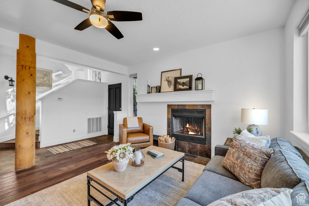 Living room with a tiled fireplace, ceiling fan, and dark wood-type flooring