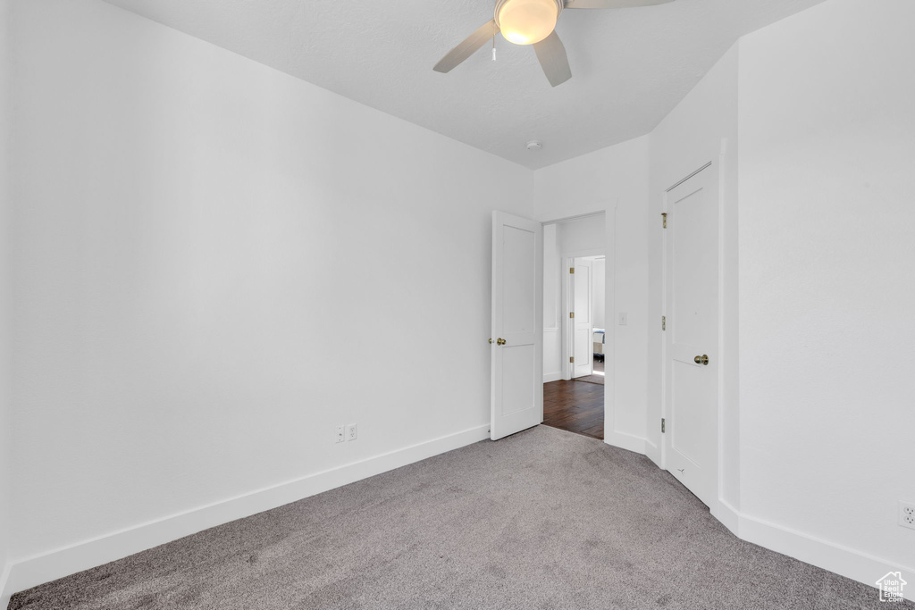 Unfurnished room with ceiling fan and dark colored carpet
