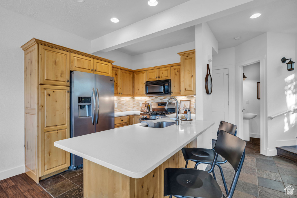 Kitchen with dark tile flooring, tasteful backsplash, appliances with stainless steel finishes, and a breakfast bar