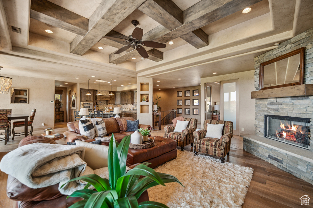 Living room featuring coffered ceiling, a tray ceiling, ceiling fan with notable chandelier, dark wood-type flooring, and a fireplace