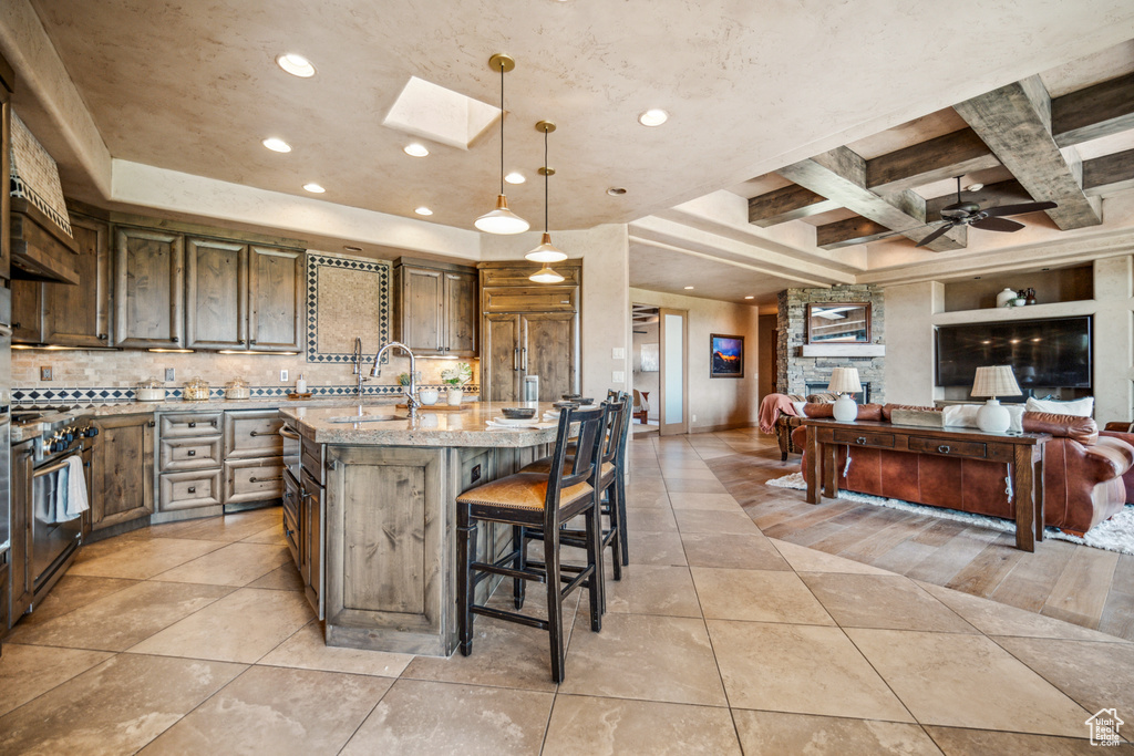 Kitchen featuring pendant lighting, a fireplace, a kitchen bar, ceiling fan, and a kitchen island with sink