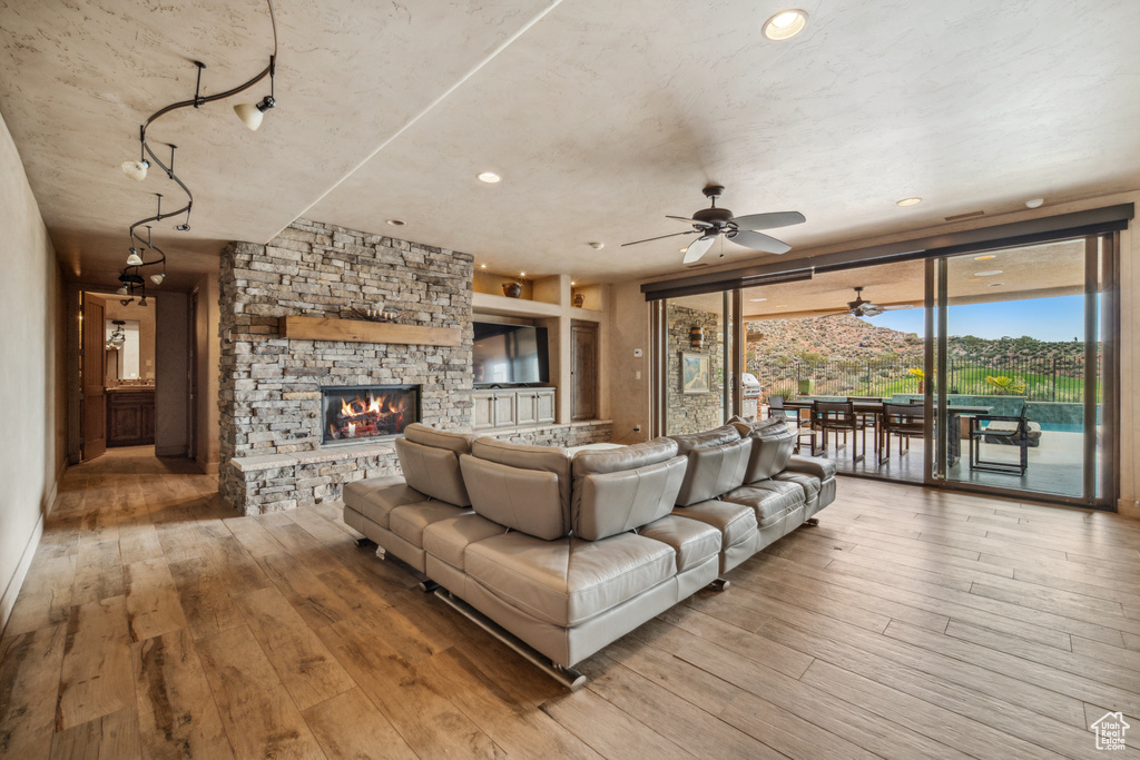 Living room with a stone fireplace, ceiling fan, and light wood-type flooring