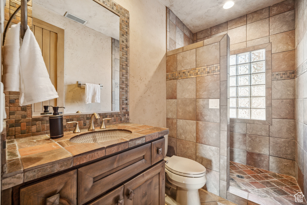 Bathroom featuring tile walls, walk in shower, toilet, and vanity