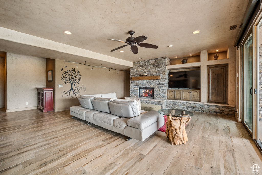 Living room featuring a stone fireplace, light hardwood / wood-style floors, and ceiling fan