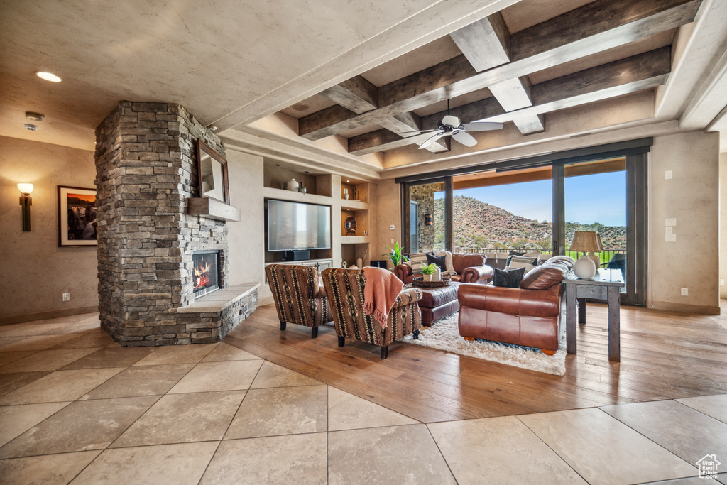 Tiled living room featuring a stone fireplace, ceiling fan, and beamed ceiling