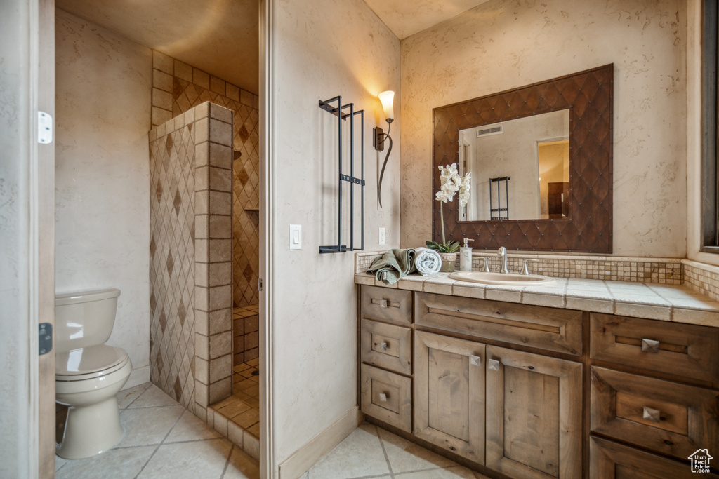 Bathroom with tile floors, toilet, a tile shower, and vanity
