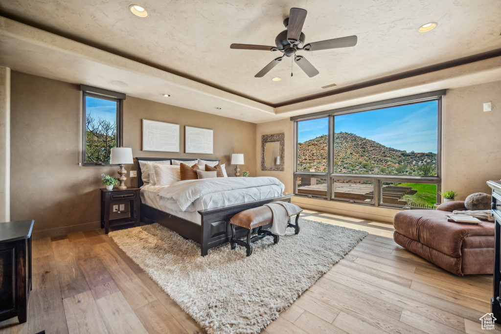 Bedroom with light hardwood / wood-style flooring, ceiling fan, and multiple windows