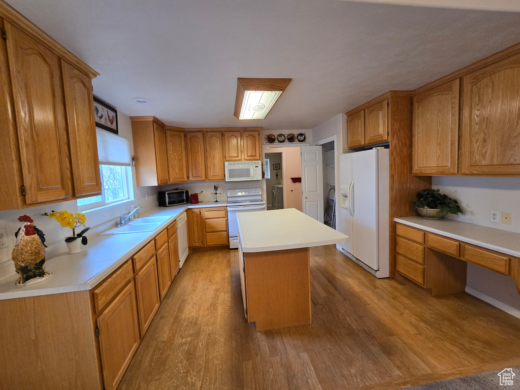 Kitchen with light hardwood / wood-style flooring, white appliances, sink, and a center island