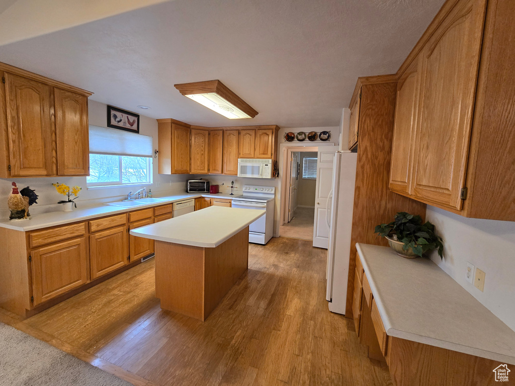 Kitchen featuring light hardwood / wood-style flooring, a kitchen island, white appliances, and sink