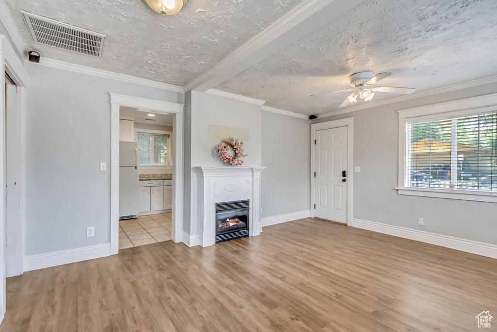 Unfurnished living room with light hardwood / wood-style flooring, a textured ceiling, ceiling fan, and ornamental molding