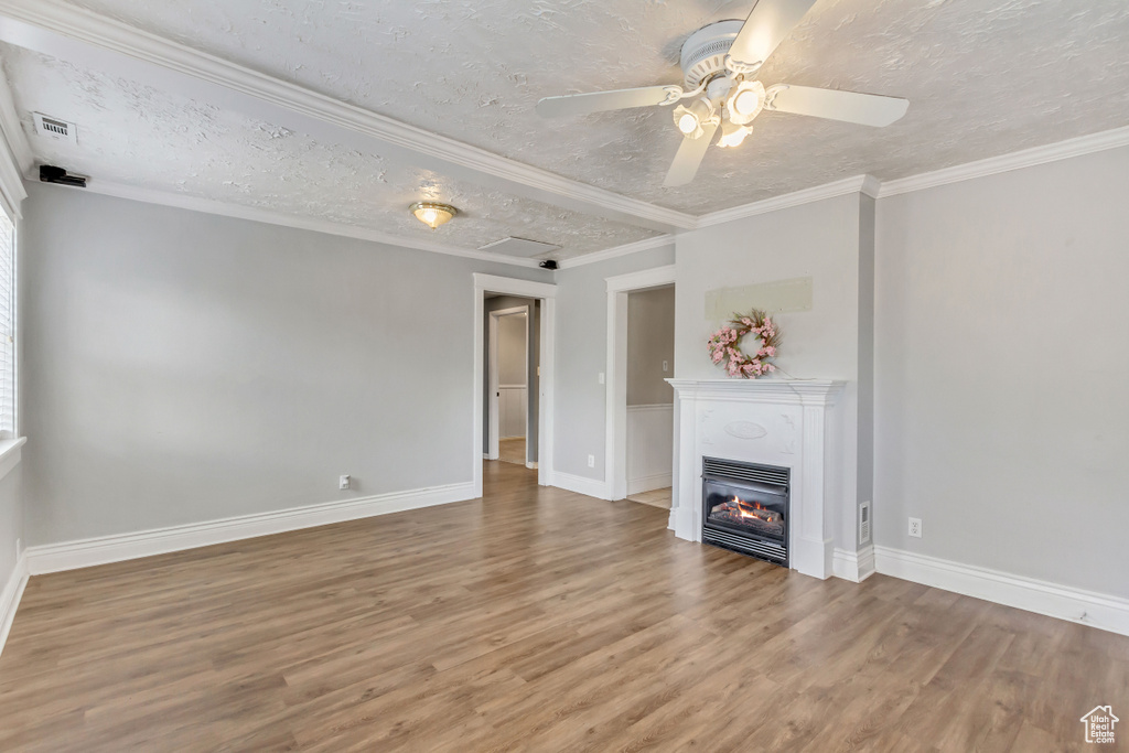 Unfurnished living room featuring a textured ceiling, ornamental molding, wood-type flooring, and ceiling fan