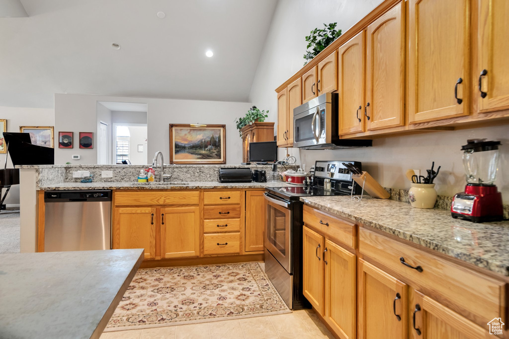 Kitchen featuring sink, light tile floors, stainless steel appliances, vaulted ceiling, and light stone countertops