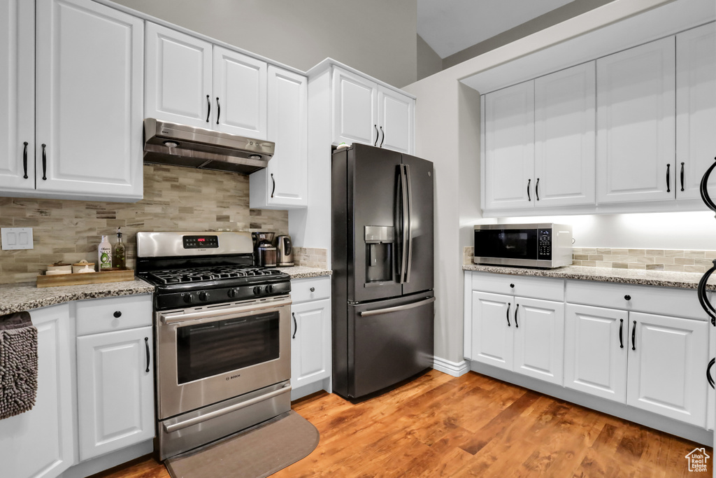 Kitchen with light stone countertops, light hardwood / wood-style flooring, appliances with stainless steel finishes, white cabinetry, and backsplash